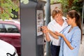 Pleasant middle aged woman helping young girl to buy ticket for street parking in modern parking meter Royalty Free Stock Photo