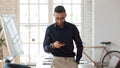 Pleasant millennial arabic businessman using smartphone at modern workplace.