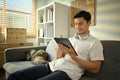 Pleasant millennial man resting on couch at home and using digital tablet