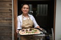 Pleasant multiethnic cute woman, smiling housewife holding a baking sheet with raw pizza before putting it in the oven