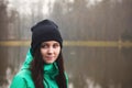 Pleasant and pretty brunette in winter jacket looking into the camera at a small pond near Opava, Czech Republic. Candid portrait