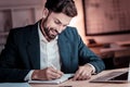 Pleasant satisfied man smiling and writing in his notebook.