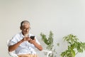 Pleasant senior older men resting while sitting on chair, Asian elder man with grey hair using application on smartphone at home Royalty Free Stock Photo
