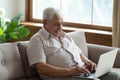 Pleasant senior 70s man sitting on sofa with computer.