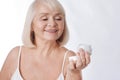 Pleasant senior woman looking at the cream bottle