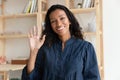 Pleasant smiling biracial woman making hello gesture, looking at camera.