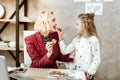 Pleasant smiling light-haired little girl feeding her giggling mother