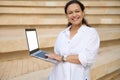 Pleasant smiling young woman looking at camera, holding laptop with white mockup digital screen. Copy advertising space