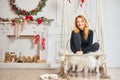 A pleasant sweet girl with red hair sits near the New Year`s fireplace. Holiday concept at home