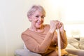 Pleasant thoughtful aged woman seating with a walking stick. Retired woman with her wooden walking stick at home. Happy senior Royalty Free Stock Photo