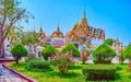 The pleasant walk in a shadow of lush trees of a small garden with a view on Dusit Maha Prasat Throne Hall of Grand Palace, on May