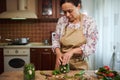 Pleasant multiethnic woman in a chef& x27;s apron preparing pickled cucumbers in the home kitchen interior. Pickling