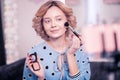 Pleasant woman putting some face powder while doing makeup