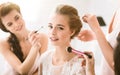 Pleasant young bridesmaids helping the bride to get ready