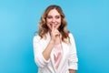 Please, be quiet! Portrait of positive lady smiling and making hush sign with finger on lips. studio shot, blue background Royalty Free Stock Photo