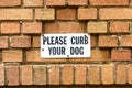 Please Curb Your Dog sign affixed to a brick building wall. Close up