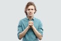 Please help me. Portrait of hopeful handsome long haired blonde young man in blue shirt standing with palm hand and hope for help