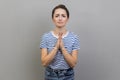 Woman holding hands in prayer and asking for help with pleading imploring expression, full of hope.