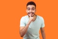 Please, keep silence! Portrait of positive brunette man asking to be quiet. indoor studio shot isolated on orange background