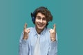 Please. Portrait of a young beautiful man wearing white t-shirt and blue shirt in blue headphones holding his fingers crossed