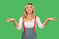 Please, take for free! Portrait of friendly generous adult blond woman in overalls holding up hands and welcoming