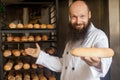 Please take it. Portrait of attractive positive young adult baker with long beard in white uniform standing in his workplace and Royalty Free Stock Photo