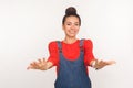 Please, take it! Portrait of positive stylish girl with hair bun in denim overalls inviting to embrace, keeping hands as giving