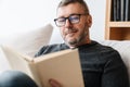 Pleased adult unshaven man reading book while resting