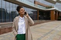 pleased african american young woman talking on mobile phone against glass business center Royalty Free Stock Photo