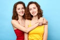 Pleased awesome twins wearing t-shirts hugging each other and looking at the camera over blue background