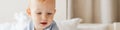 Pleased blonde baby boy looking at tablet computer while playing on bed