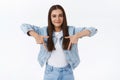 Pleased, boastful cute happy brunette girl in denim jacket with sassy, satisfied smile, pointing fingers down and gazing
