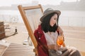 Pleased brunette girl resting in recliner with eyes closed. Smiling dark-haired woman enjoying cocktail during weekend