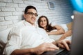 Pleased businessman is typing on laptop. Young woman lies in bed with businessman. Royalty Free Stock Photo