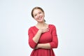 Pleased caucasian woman wearing bred dress smiling broadly and keeping hand on her chest,