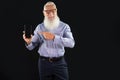 Pleased elderly handsome senior businessman with white beard holding mobile phone with blank empty screen, pointing on device,