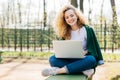 Pleased European woman having beautiful fluffy blonde hair wearing jeans, jacket and sport shoes sitting crossed legs using