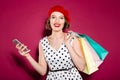 Pleased ginger woman in dress holding packages and smartphone