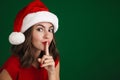 Pleased girl in Santa Claus hat showing silence gesture on camera Royalty Free Stock Photo