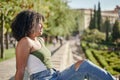 Pleased happy cute young student curly girl sitting on bench outdoors in nature park with beautiful sunlight Royalty Free Stock Photo