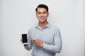 Pleased happy young asian man holding smartphone pointing at cellphone screen as showing awesome new phone Royalty Free Stock Photo