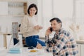 Pleased husband and wife manage finances at home, review bank accounts, pleased man holds mobile phone near ear, wears plait shirt Royalty Free Stock Photo