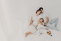 Pleased husband, wife and their small daughter pose in spacious bedroom with favourite pet, have fun, embrace and express love to