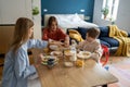 Pleased kid boy holds spoon cocoa while mom and teen sister want drink coffee. Family breakfast time