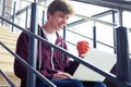 Pleased male holding cup of coffee and chatting in laptop