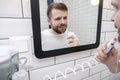 Pleased man cleans his teeth with the help of electric oral irrigator with a jet of water, looking in the mirror. Royalty Free Stock Photo