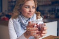 Pleased mature woman holding hot cup of tea to warm hands