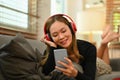Pleased millennial woman with wireless headphone lying on comfortable couch and using smart phone