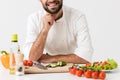 Pleased positive happy young chef isolated over white wall background in uniform cooking with fresh vegetables