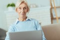 Pleased senior woman sitting at home and holding a modern laptop